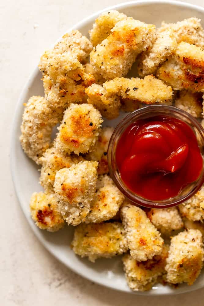 Parmesan Baked Chicken Nuggets on a white plate with a bowl of ketchup for dipping