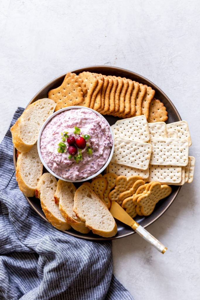 Cranberry jalapeno di[ on a white bowl on a plate with crackers and bread