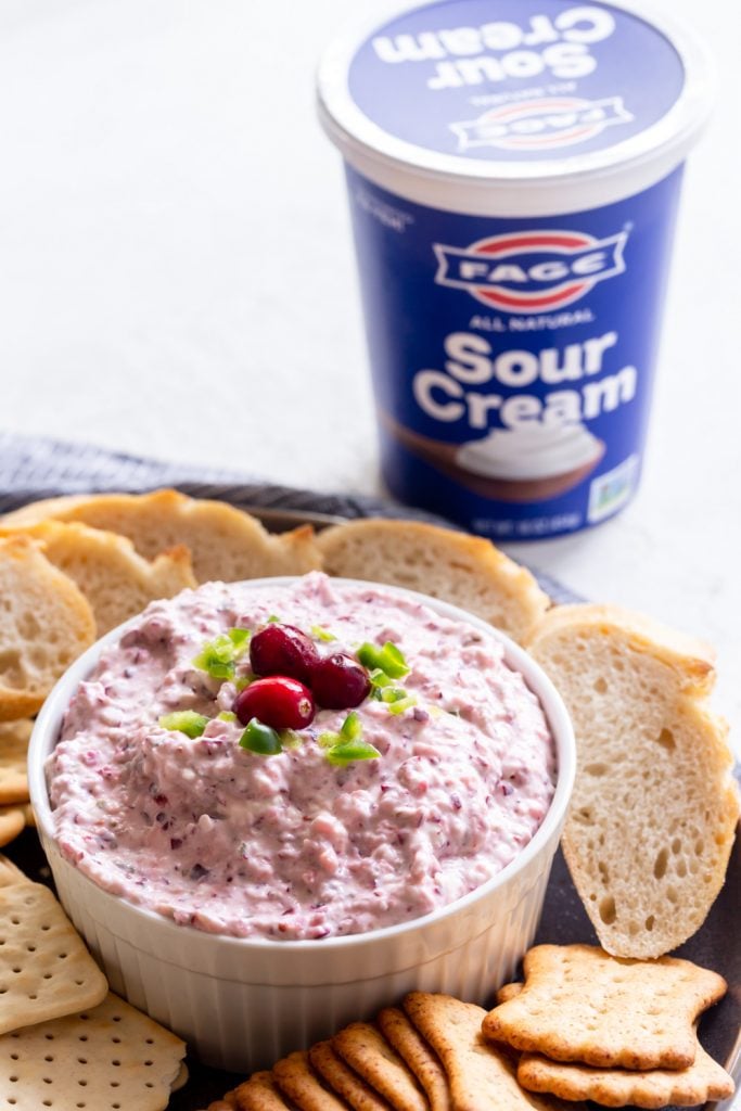 Cranberry jalapeno dip in a white bowl on a plate next to crackers and bread