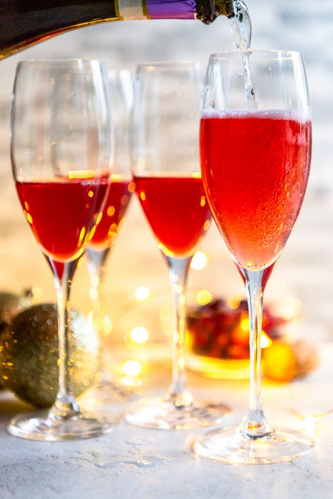 Prosecco pouring into a champagne flute with cranberry juice in it. 