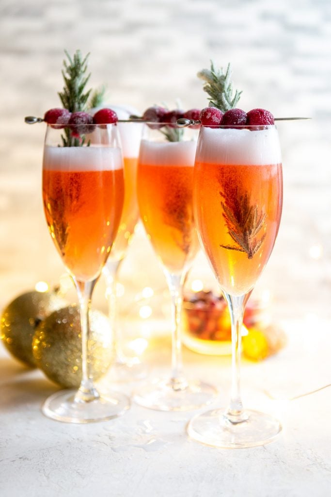 Cranberry mimosas in champagne flutes, garnished with cranberries and rosemary.