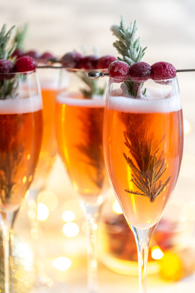 Cranberry Mimosa in a champagne flute, garnished with sugared cranberries and rosemary. 