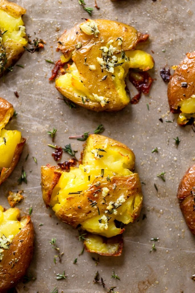 Crispy smashed potato on a baking sheet topped with garlic butter and herbs. 