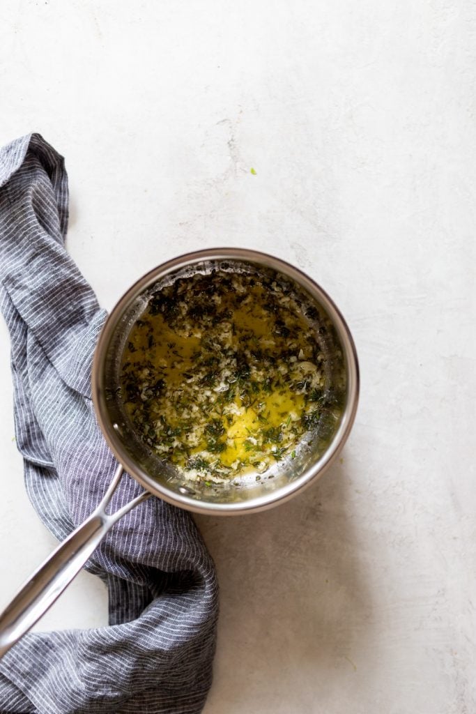 A small sauce pan of melted butter with garlic and herbs.