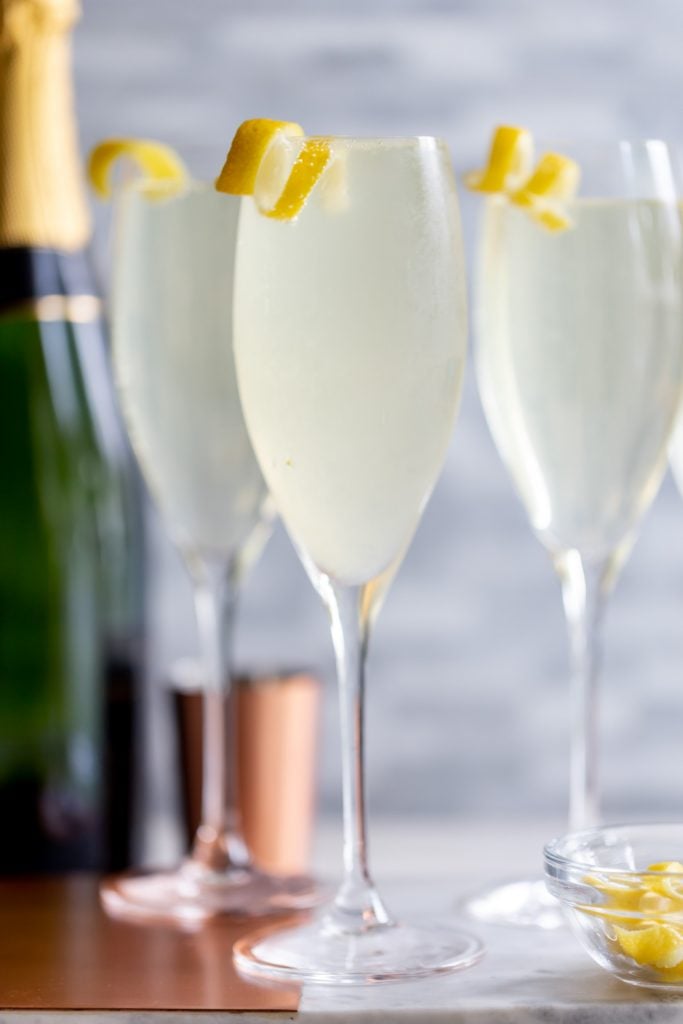 Three French 75 cocktails in champagne flutes, garnished with a lemon twist