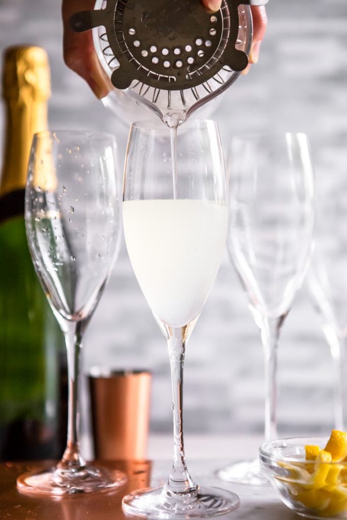 French 75 being poured from a cocktail strainer into a champagne flute
