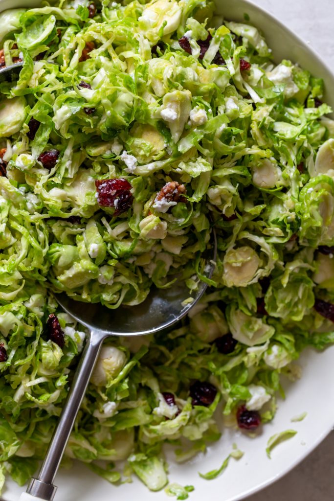 Close up of shaved brussels sprouts salad with cranberries, goat cheese, pecans and maple dressing