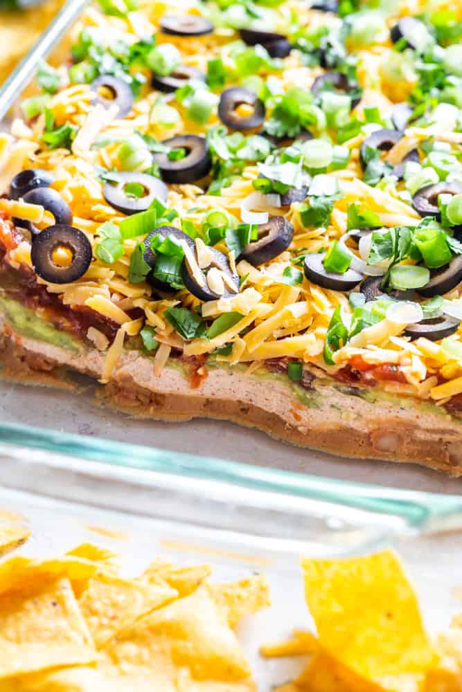 Closeup of seven layer dip showing the layers - beans, sour cream, guacamole, salsa, cheese, olives, green onions and cilantro. 