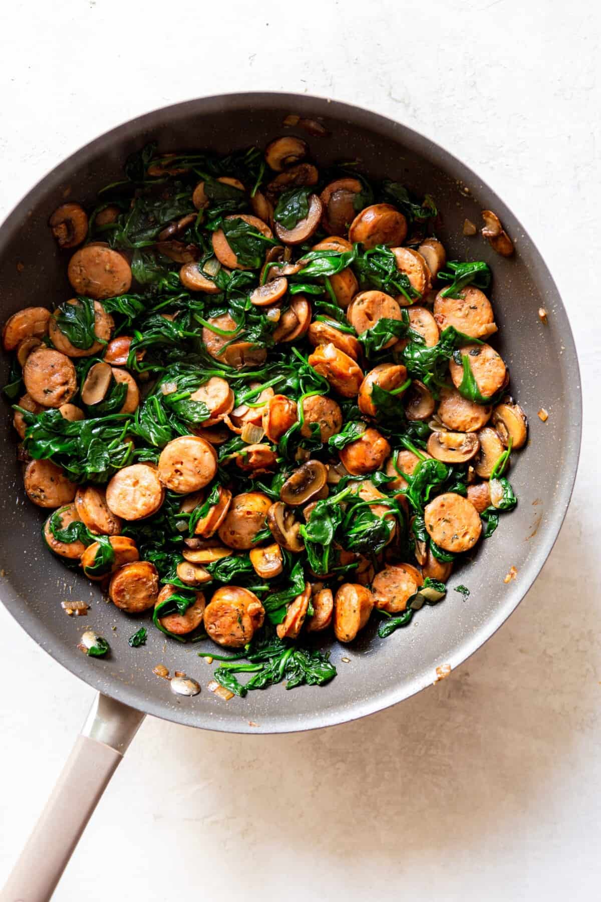 Spinach after cooking down and wilting, with sausage and mushrooms in the pan.