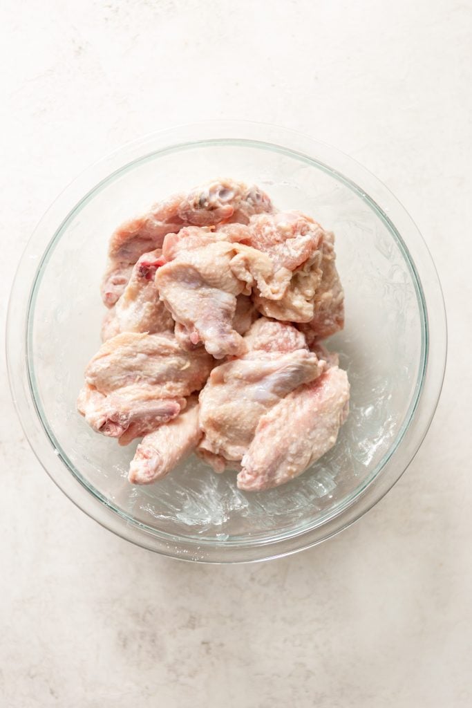Raw chicken wings in a glass bowl, tossed with baking powder and salt. 