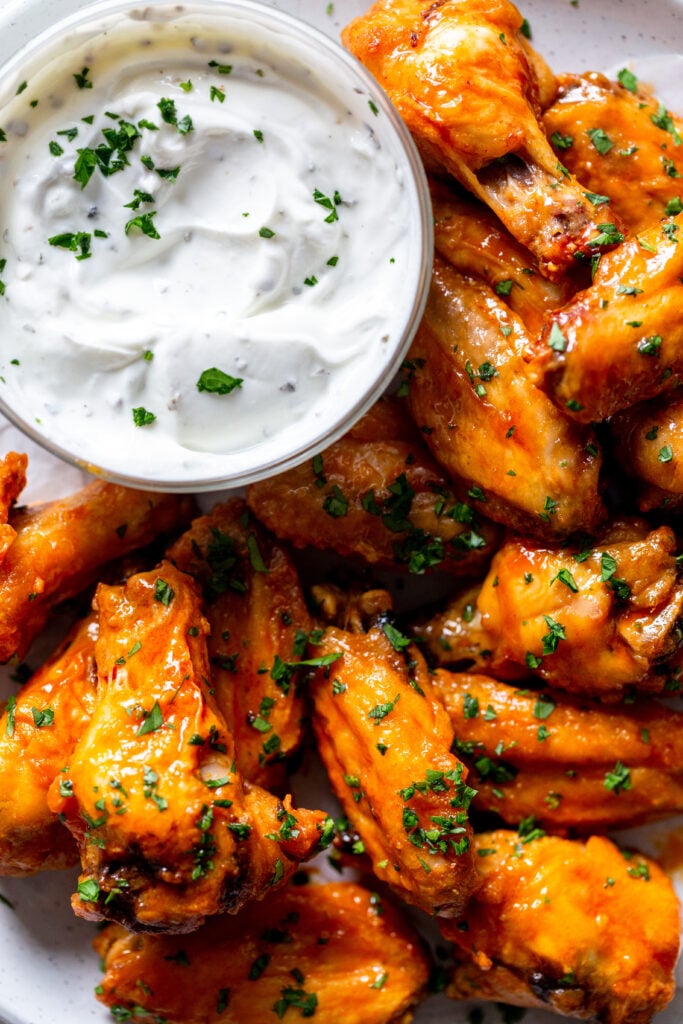 Baked buffalo wings next to a dish of creamy yogurt dip. 