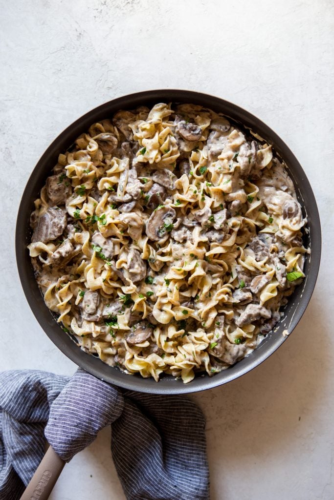Beef stroganoff with egg noodles in a large pan with a blue dish towel next to it.