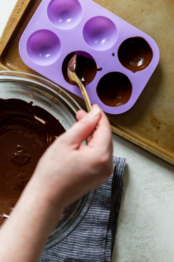 Painting melted chocolate into the sphere molds using a spoon