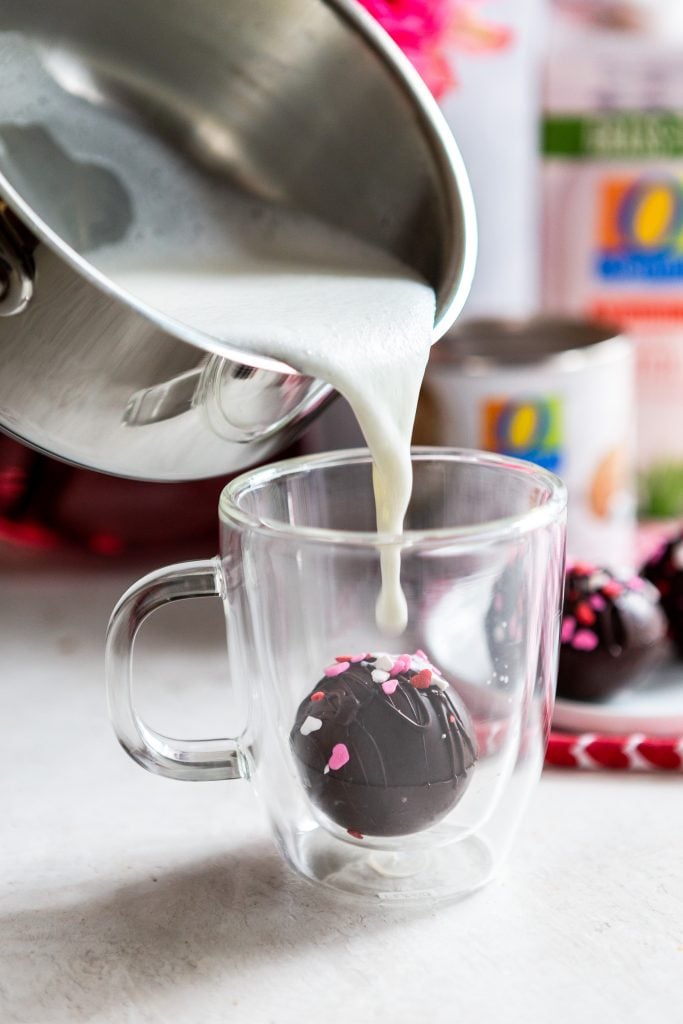 Hot chocolate bomb in a glass mug with milk about to be pored over it. 