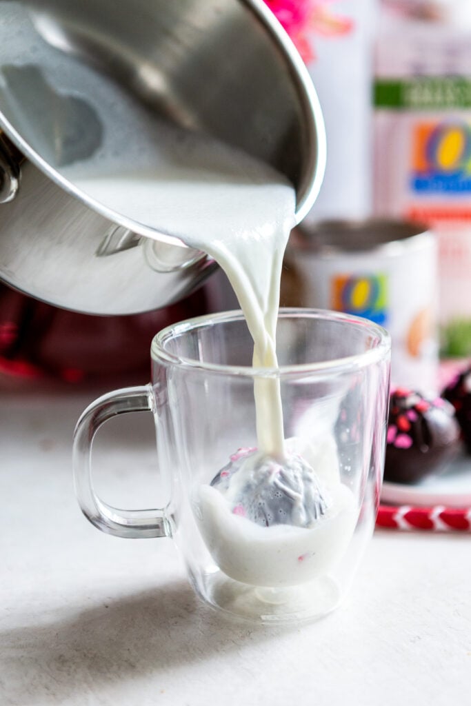 Hot milk pouring froma pan into a glass mug over the hot chocolate bomb