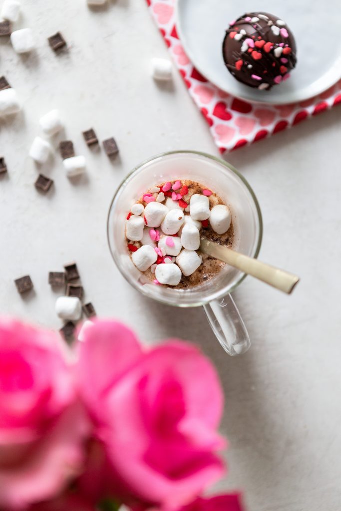Glass mug with hot chocolate, marshmallows and red and pink heart sprinkles