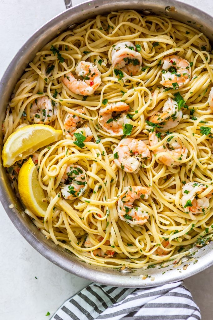 Shrimp scampi Pasta inn a stainless steel pan, with lemon wedges.