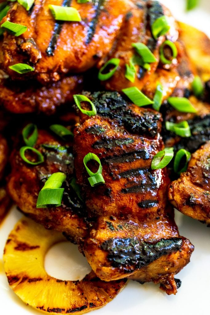 Close up of a char grilled huli huli chicken thigh, brushed with sauce, garnished with green onions. 