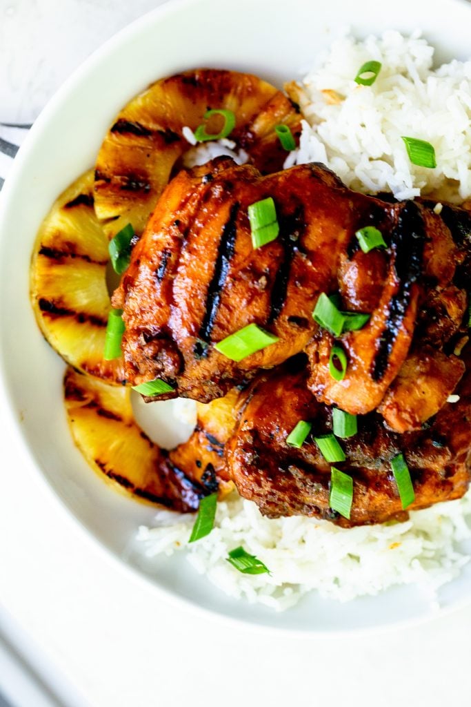 Grilled huli huli chicken on a bed of white rice with slices of grilled pineapple