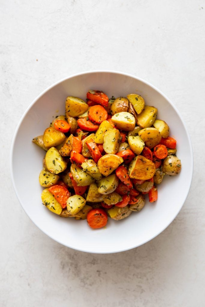 Finished roasted potatoes and carrots in a white bowl.