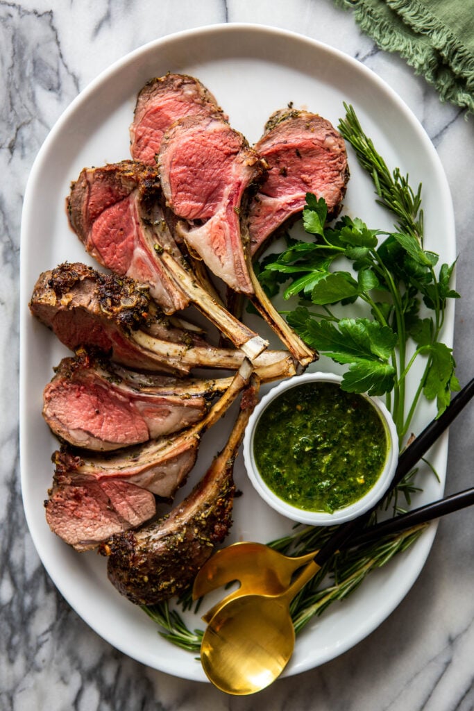 Roasted Lamb Chops on a white platter with herbs. 