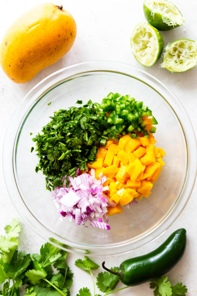 ingredients for mango salsa in a bowl. Diced mangoes, red onion, jalapeno, cilantro.