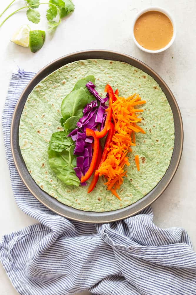 A green spinach tortilla with spinach, purple cabbage, red bell pepper and grated carrots on a grey plate.