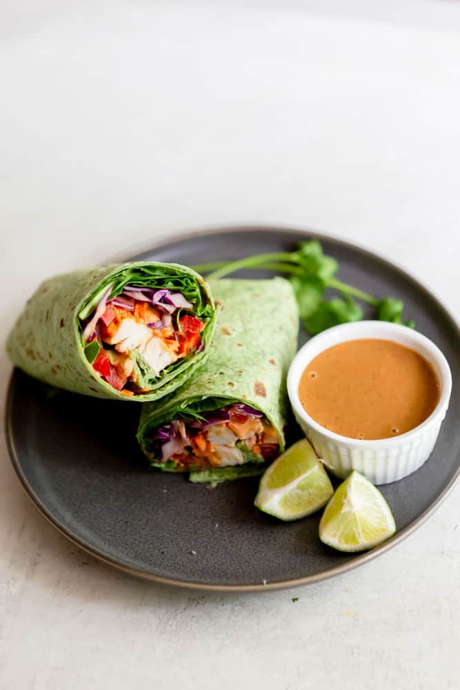 Peanut chicken wrap on a grey plate with a small dish of peanut sauce