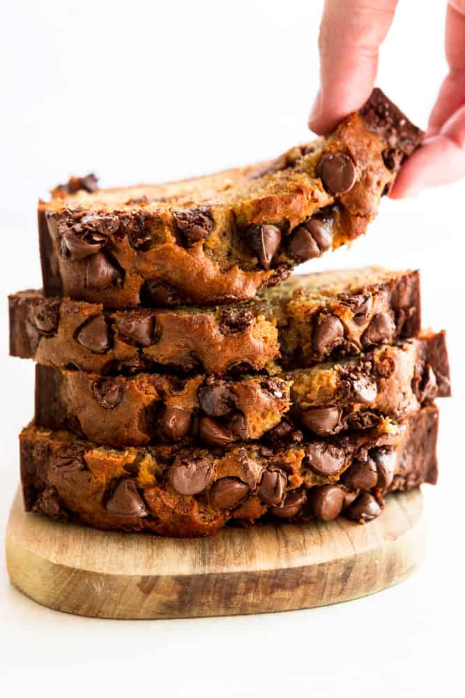 A stack of chocolate chip banana bread slices, the top one being picked up by a hand.