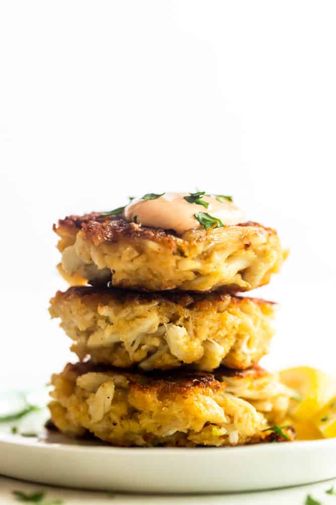Stack of three crab cakes in a white plate, topped with sriracha aioli. 