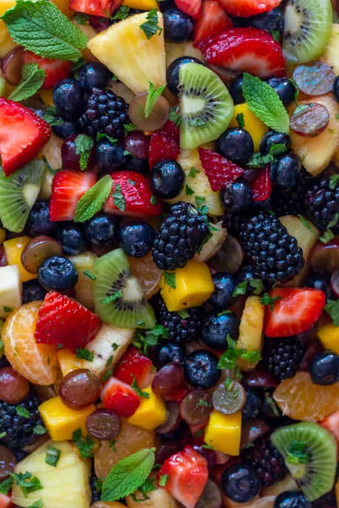 Close Up of Fruit Salad with blackberries, kiwi, strawberries, blueberries, grapes, mango, pineapple and tangerine. Garnished with mint leaves,
