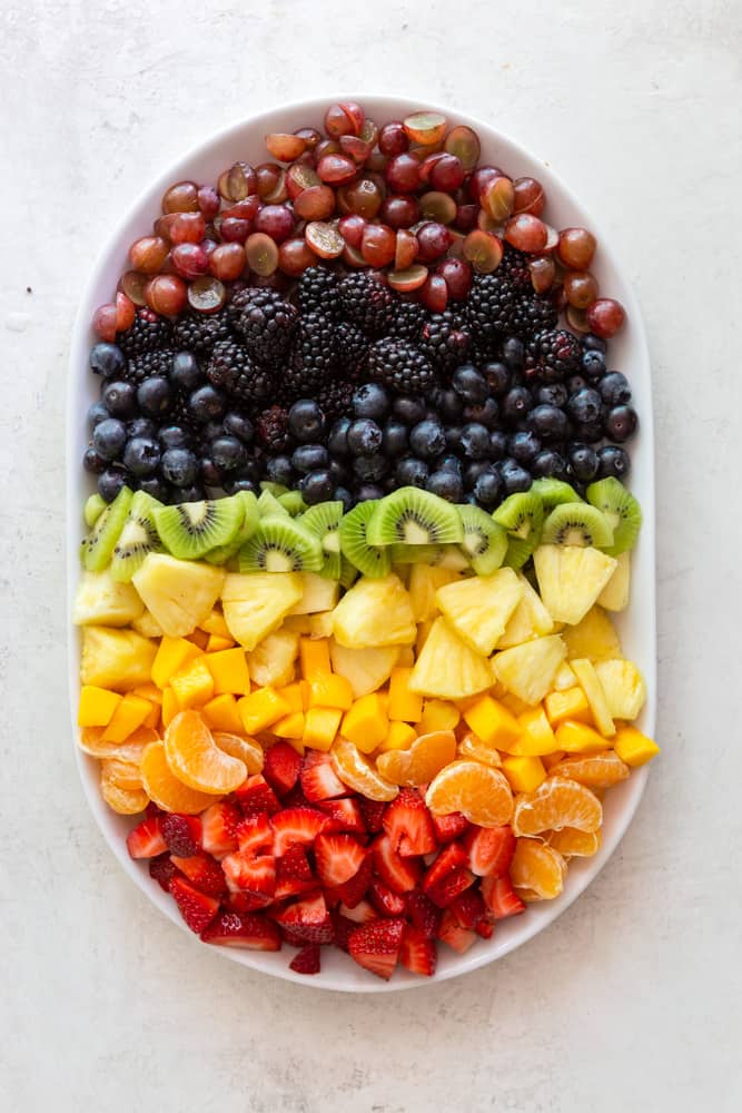 rainbow of fruits on a white platter. Grapes, blackberries, blueberries, kiwi, pineapple, mango, tangerine, strawberries.