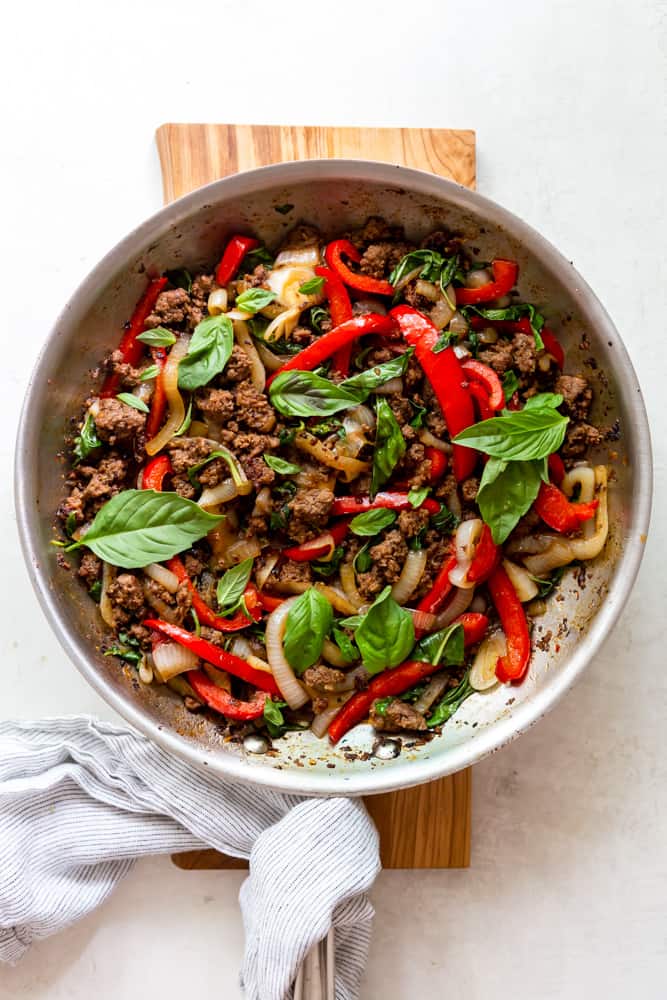 Thai basil beef in a large stainless steel skillet, garnished with fresh basil.