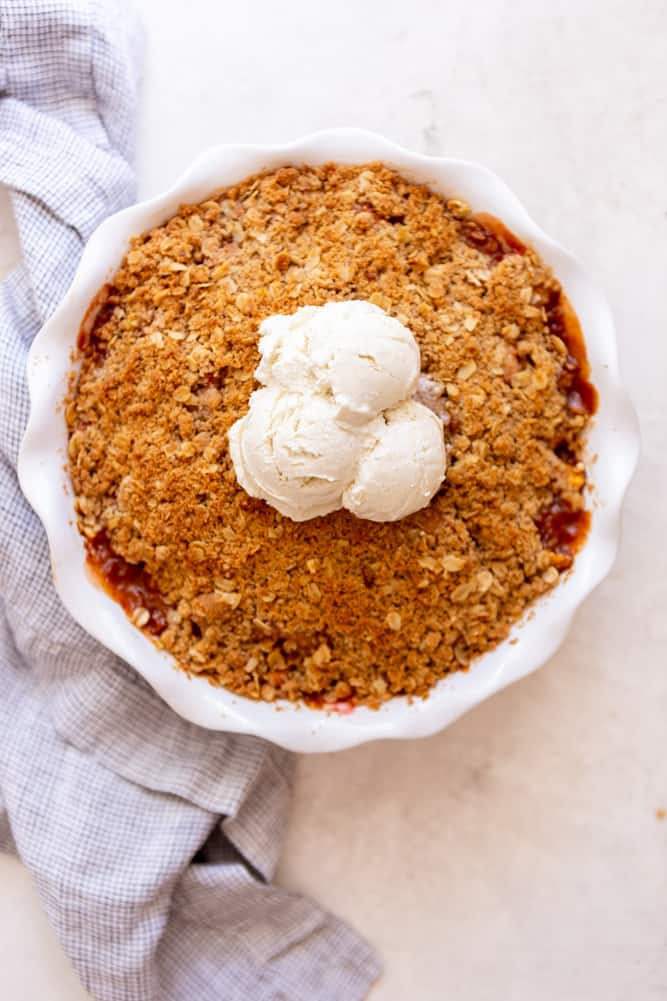 Peach crisp in white round pan, topped with ice cream.