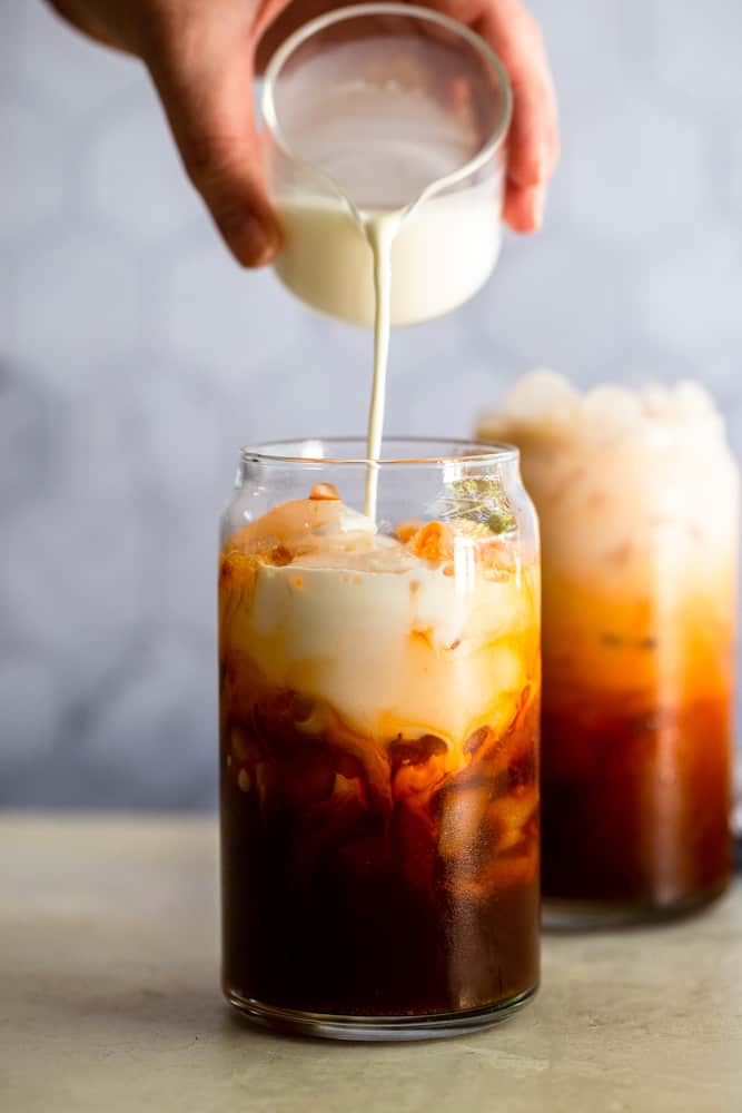 Glass of Thai iced tea with half and half pouring into it.