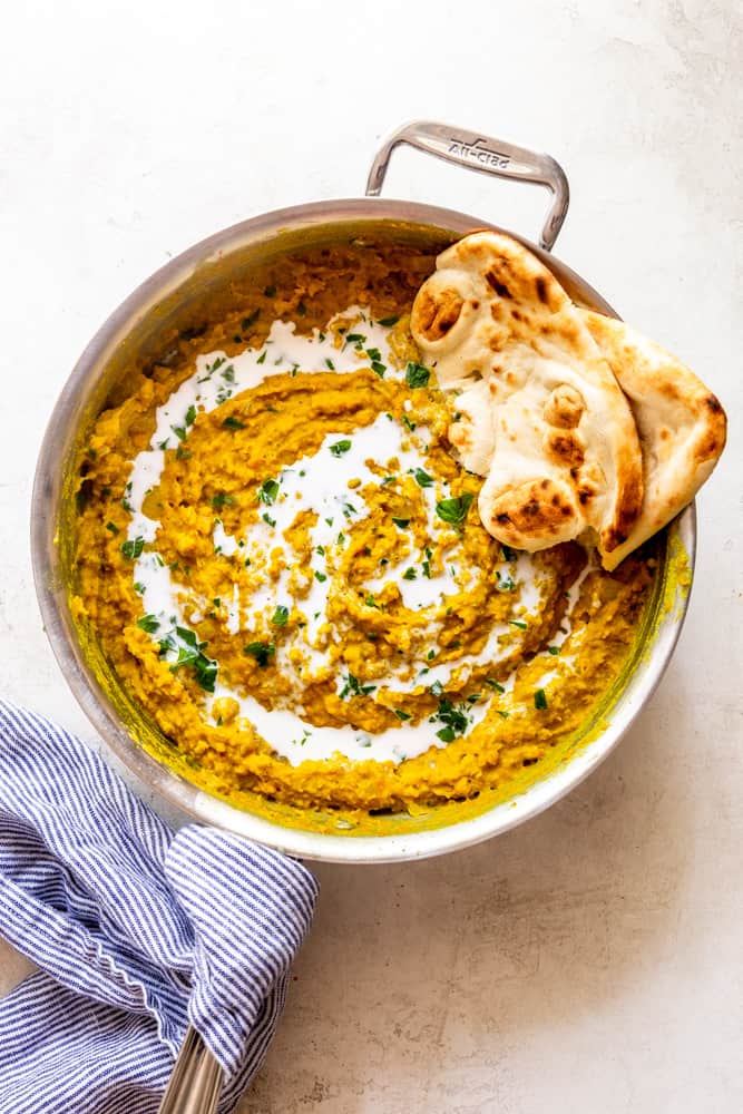A large saute pan will cooked red lentil dal, garnished with coconut milk and parsley, with a side of naan bread.