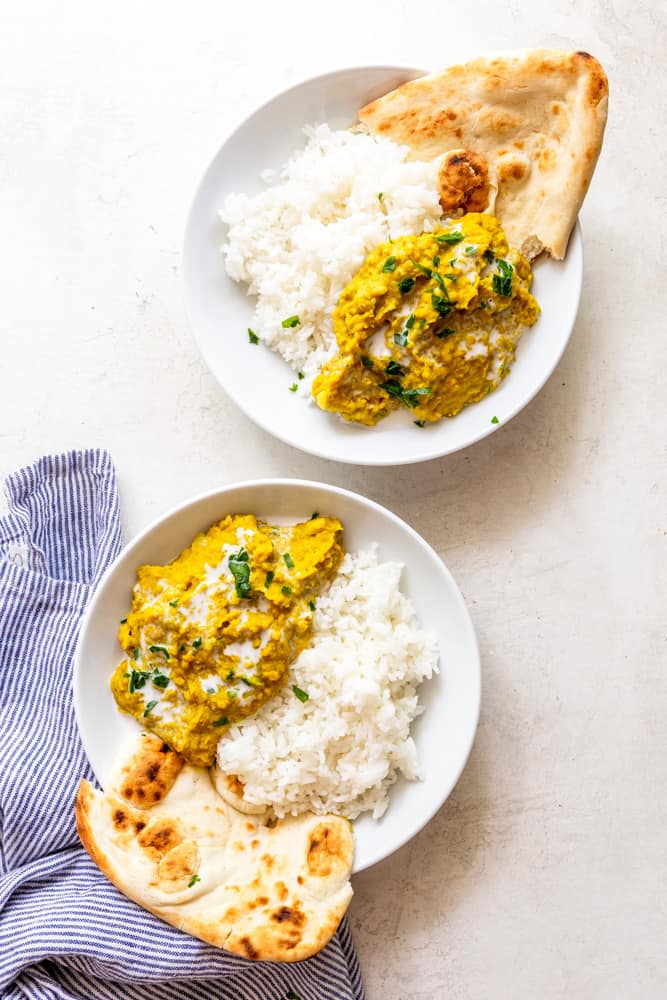 Two white bowls with lentil dal, white rice and naan.