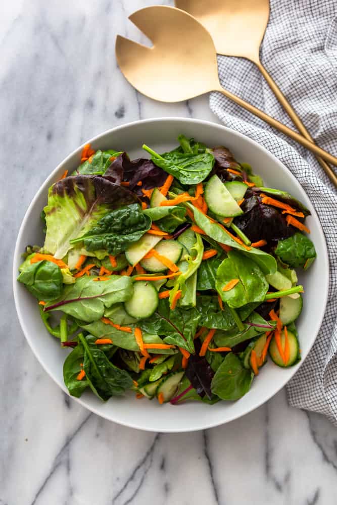 Everyday side salad with carrots and cucumbers in a white serving bowl, on a marble background.