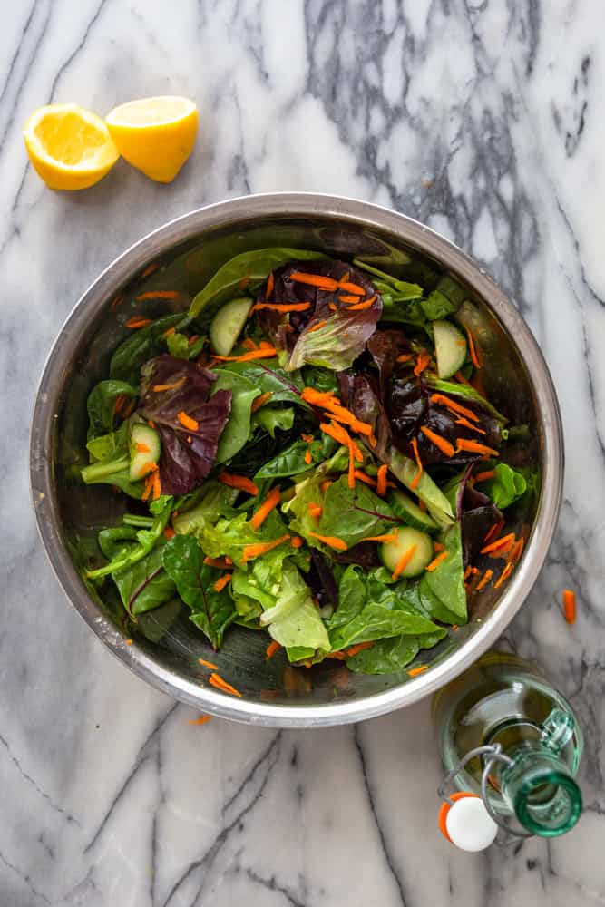 Green salad with carrots and cucumbers in a metal mixing bowl.