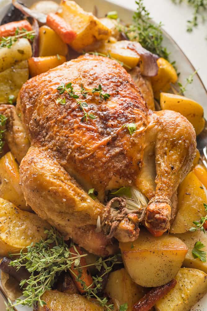 Roasted chicken with golden, crispy skin, on a bed of roasted potatoes and carrots