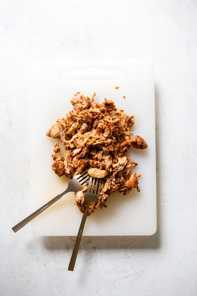Salsa chicken shredded on a cutting board with two forks.