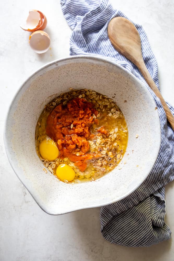 Ingredients for pumpkin baked oatmeal in a bowl - oats, eggs, milk, pumpkin, maple syrup, butter, vanilla, spices, salt and baking powder.
