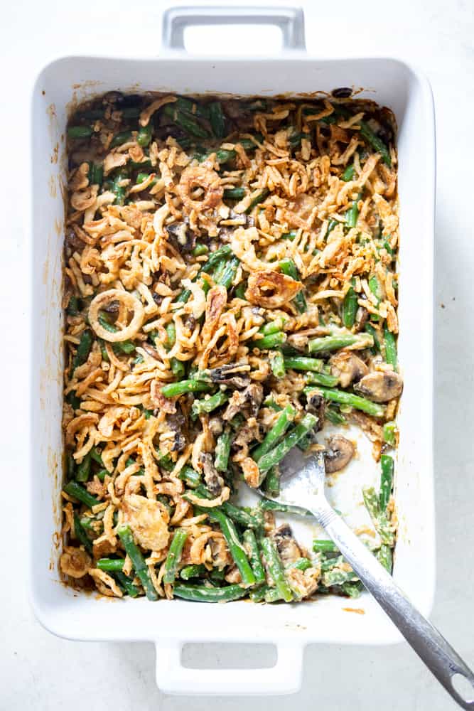 A white casserole dish with a stainless steel serving spoon scooping the green bean casserole.