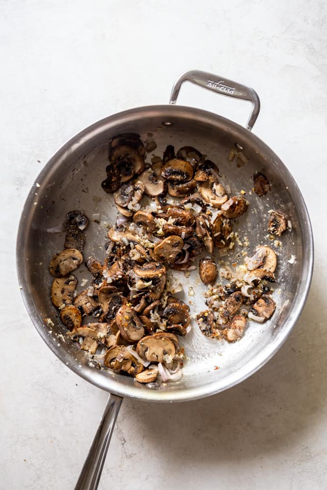 Sliced mushrooms in a stainless steel saute pan, with shallots and garlic.