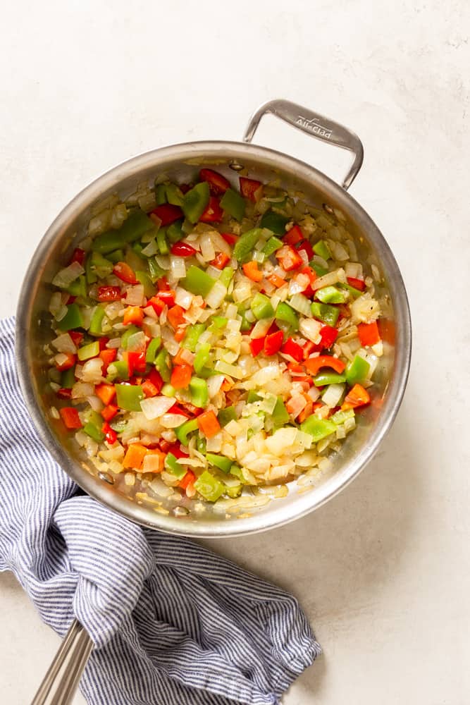 A saute pan with diced onions, red and green bell pepper, and garlic.