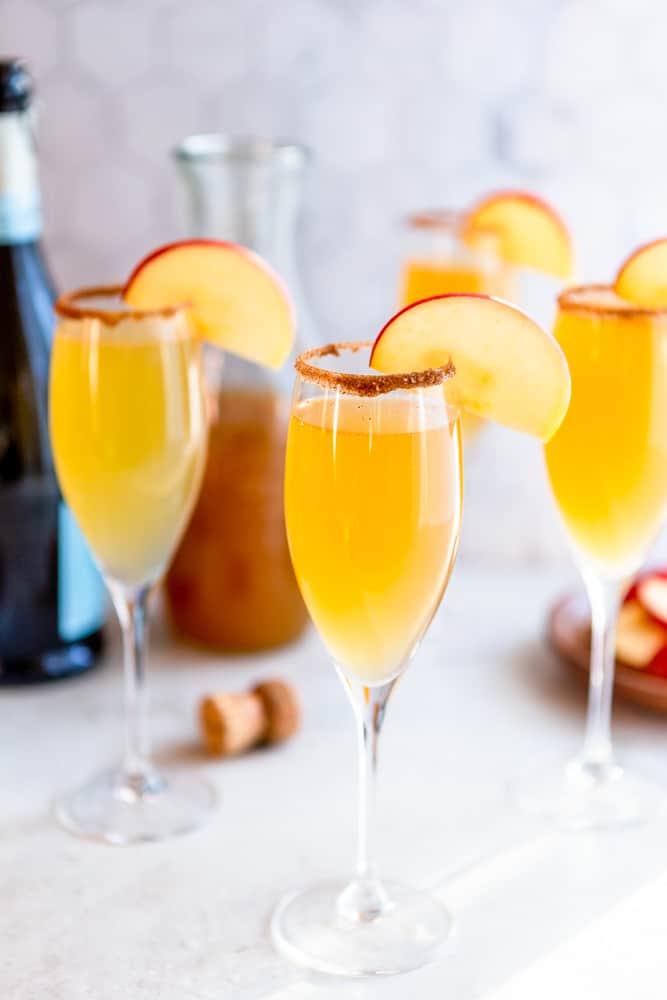 Apple Cider Mimosa in a champagne glass, garnished with a cinnamon sugar rim and an apple slice