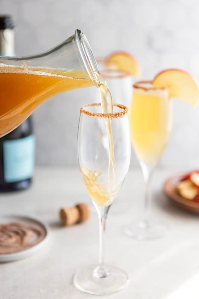 Apple cider pouring into a champagne glass with a cinnamon sugar rim.