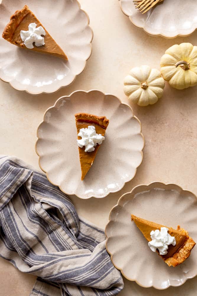 Several plates with pumpkin pie slices on them, each topped with whipped cream.