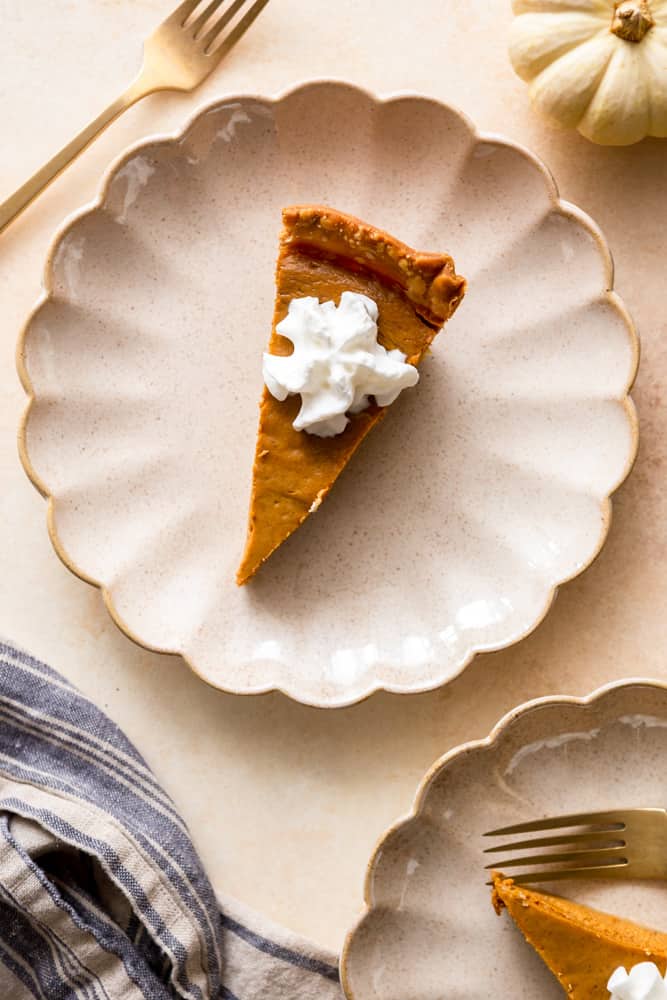 A slice of pumpkin pie topped with a dollop of whipped cream on a scalloped, off white plate.