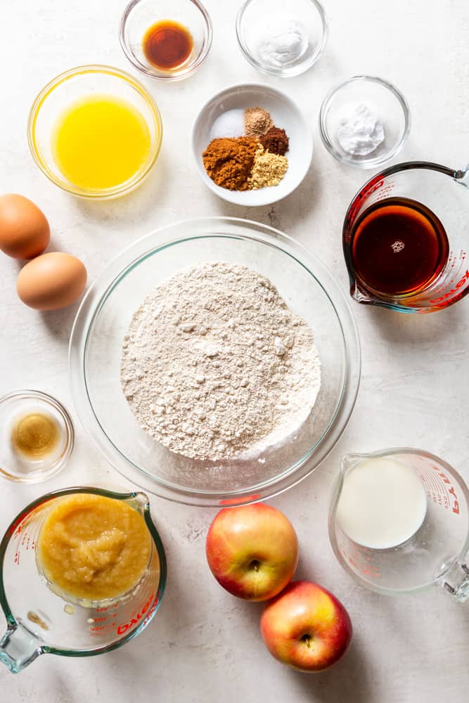 Ingredients for healthy apple muffins - apples, applesauce, apple cider vinegar, eggs, butter, vanilla, spices, baking powder, baking soda, maple syrup, milk.